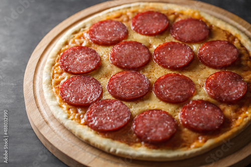 Pepperoni pizza uncut on wooden stand on dark background, selective focus.