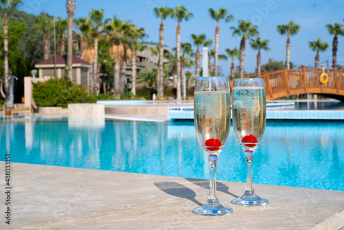 champagne glasses with cherry near the pool, blue water, sun, vacation, palms.