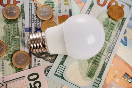 Led bulb and coins - photo on cash bank notes. Led white bulb coins is laying on cash bank notes. Electricity saving concept. Expensive light prices. Electric lamp financial budget in Europe and USA.