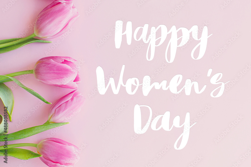 Happy womens day text on pink tulips flat lay on pink background. Stylish greeting card. International Women's Day. 8 march. Handwritten lettering