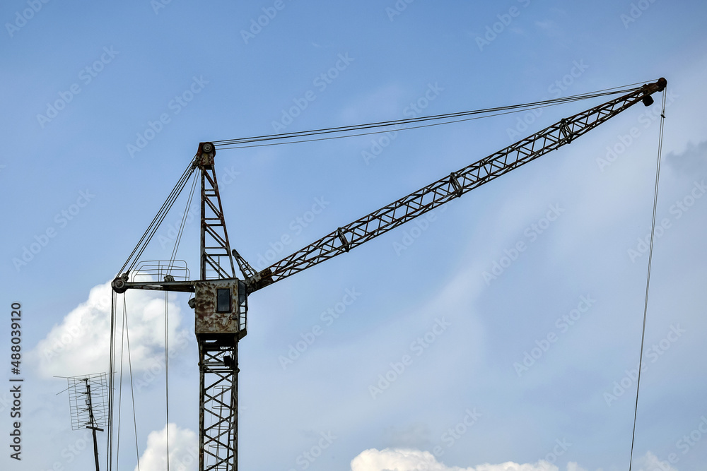 High-rise industrial tower crane with rusty cabin against blue sky with fluffy clouds. Construction site. Copy space. Selective focus. High-rise industrial tower crane with rusty cabin against blue sky with fluffy clouds. Construction site. Copy space. Selective focus.