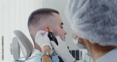 An otorhinolaryngologist examines the auricle of a patient using medical mirror