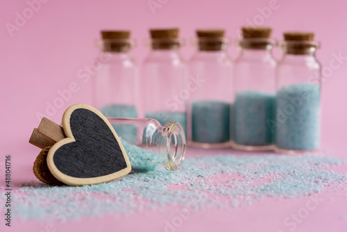 Botellitas de cristal con tapa de corcho llenas de piedritas esparcidas color turquesa con fondo rosado y clip en forma de corazón negro
