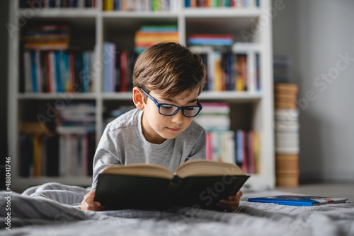 One caucasian boy lying on the floor at home in day reading a book front view wearing eyeglasses copy space real people photo