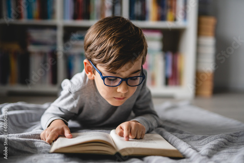 One caucasian boy lying on the floor at home in day reading a book front view copy space real people education concept