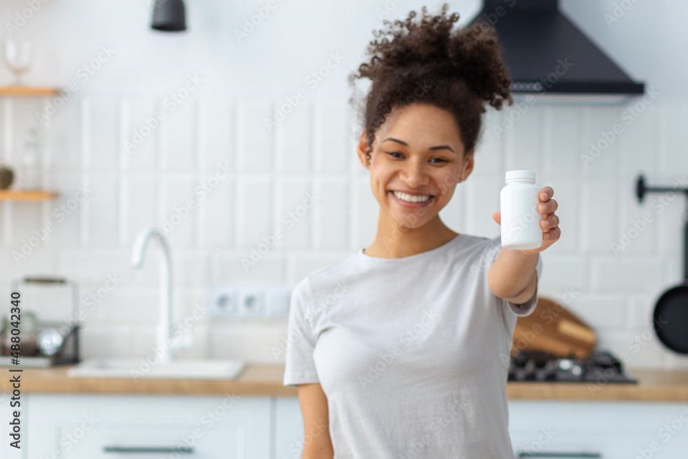 Happy young African American woman holding bottle of dietary supplements or vitamins in her hands. Close up. Healthy lifestyle concept Happy young African American woman holding bottle of dietary supplements or vitamins in her hands. Close up. Healthy lifestyle concept