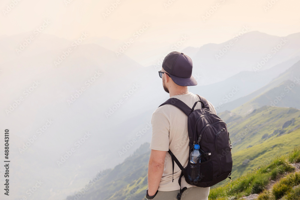 A bearded traveler with a backpack on the top of a mountain. A tourist with a backpack stands the background of a mountain. 