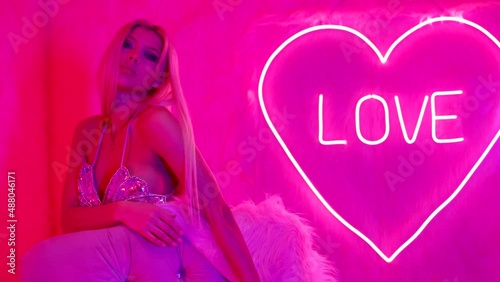 sexy woman in nightclub with pink neon lights, tempting busty blonde is looking seductively at camera