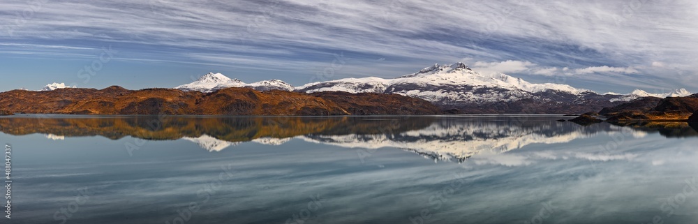 Ultra wide panorama of a landscape with snow covered mountains reflecting in a lake (Lago Pehoe) in Patagonia, Chile