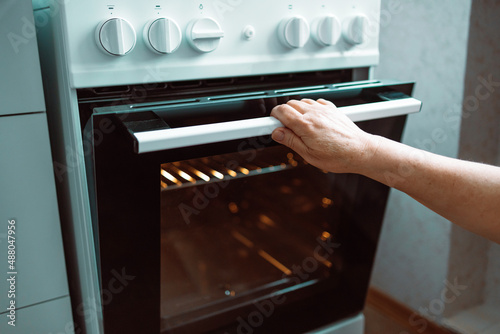 Woman hand opening oven door and light is on in kitchen at home.