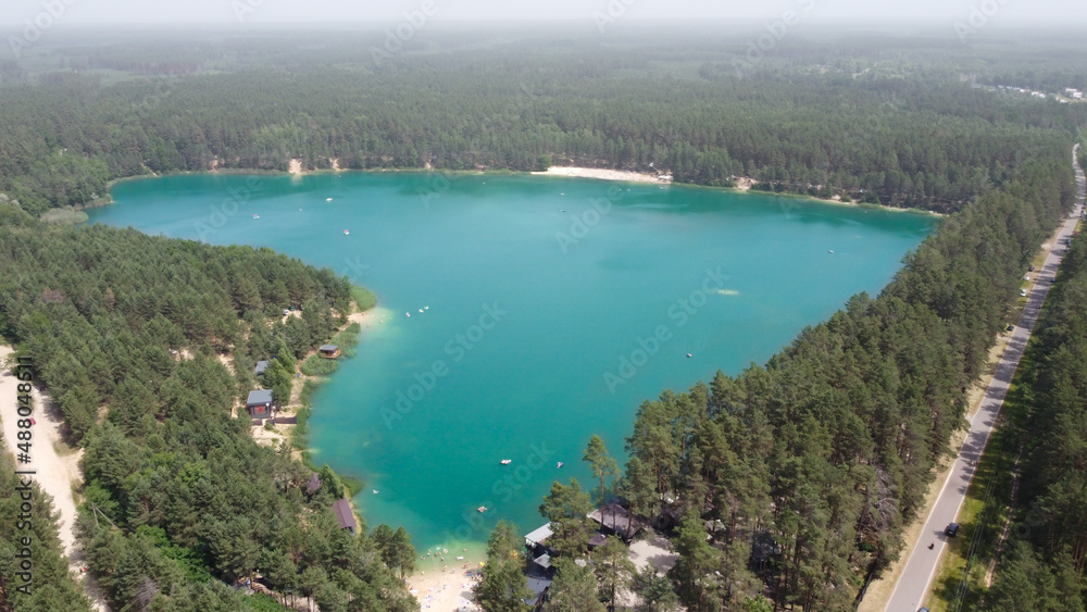 Beautiful Blue Lake looks as heart-shaped, dron photo. Aerial view of romantic nature blue lough with beach between green forests on sunny summer day with aerial perspective, Ukraine, bird's-eye view.