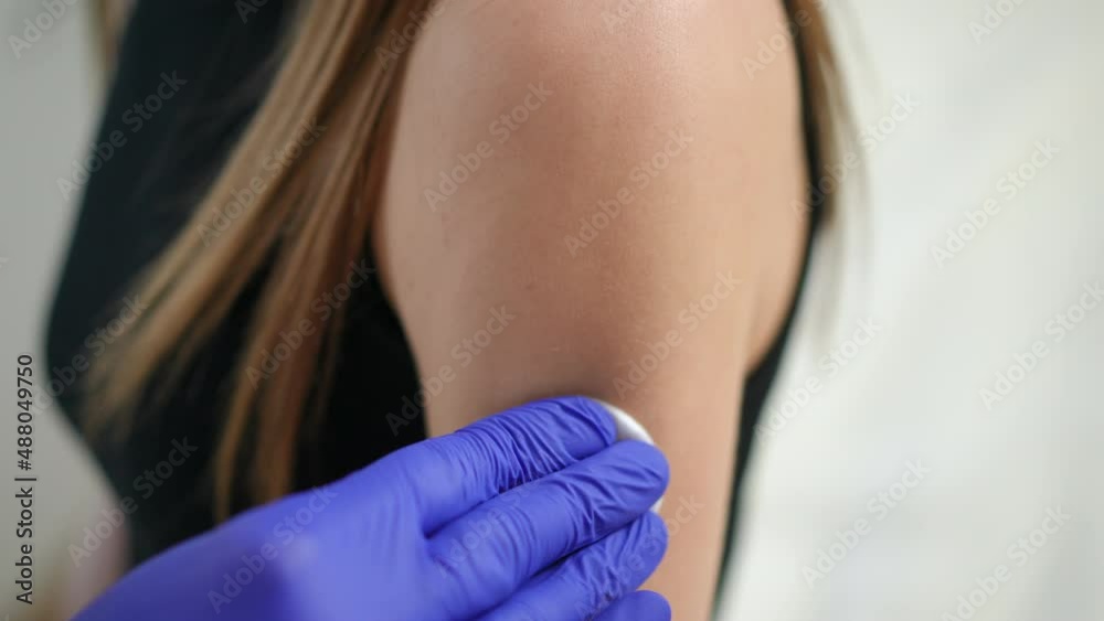 Close-up applying disinfectant on female hand before vaccination. Young slim Caucasian woman getting Covid-19 vaccine in vaxx center indoors Close-up applying disinfectant on female hand before vaccination. Young slim Caucasian woman getting Covid-19 vaccine in vaxx center indoors