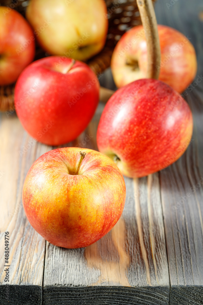 Fresh red yellow apples Gala falling from wicker basket on wooden table.