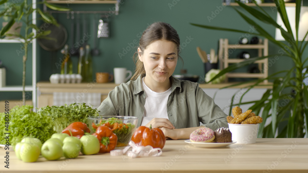 A Woman in the Kitchen Chooses Between Healthy Organic Food and Glazed Donuts.