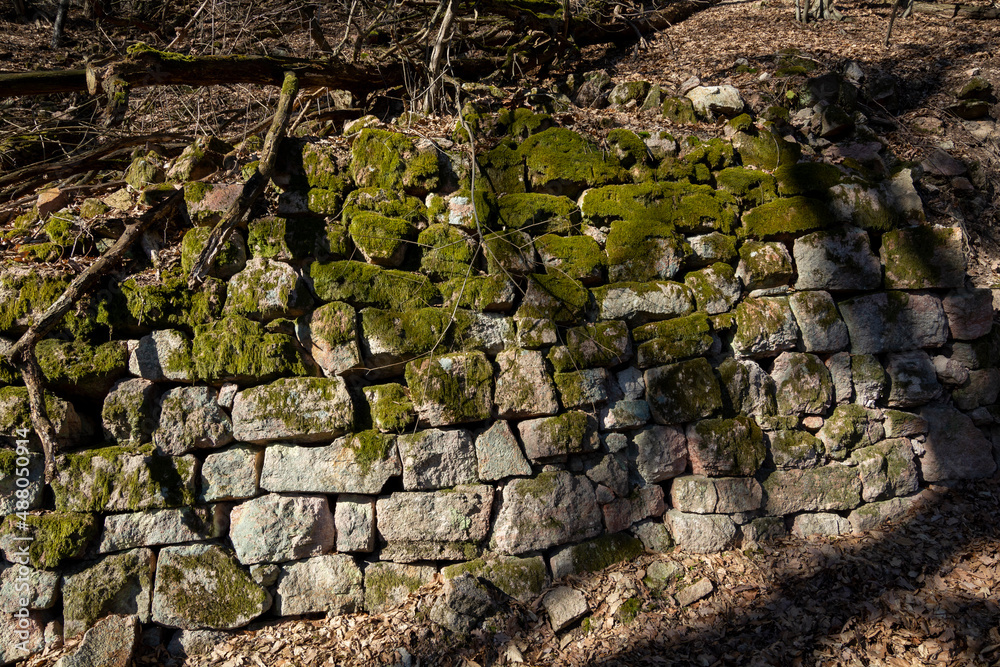 Ancient fragments of rock wall in the forest protecting road from landslide. Stone barrier.