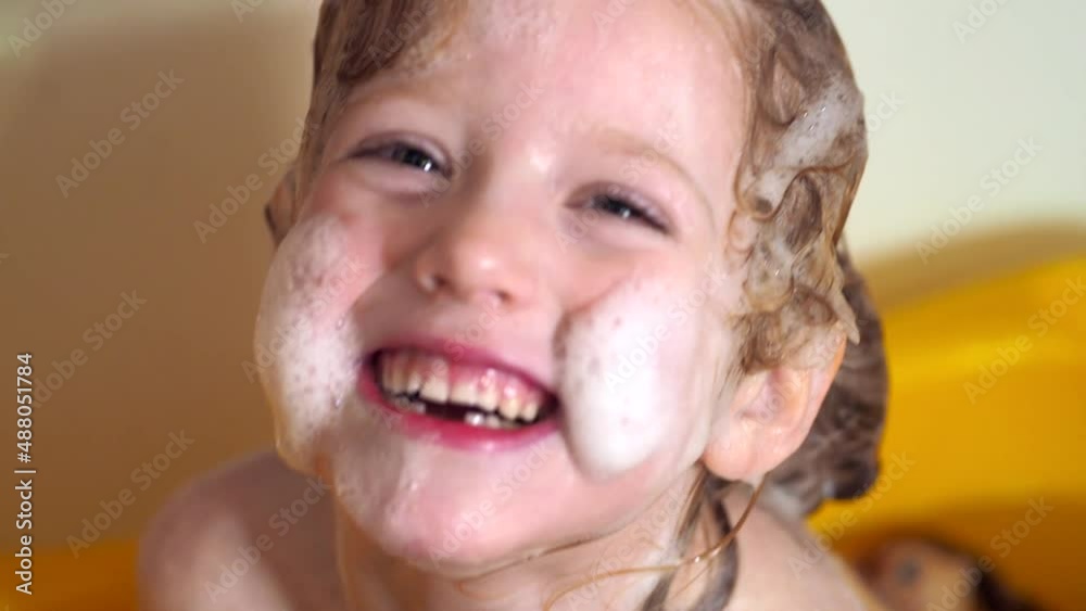 Happy child girl bathes all in foam. The child laughs while bathing in foam.