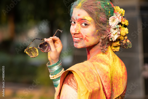 Holi festival of color, a beautiful young girl woman lady in indian attire saree with dry organic color or colour or gulal or abeer or Holi powder on face playing celebrating enjoying holi