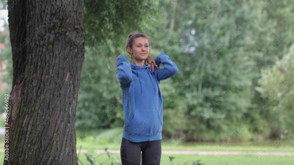 a woman in the park does sports, jogging and warming up in a public place, a millennial woman in a blue hoodie runs and squats to strengthen the body. meditation and breathing practices outdoor a woman in the park does sports, jogging and warming up in a public place, a millennial woman in a blue hoodie runs and squats to strengthen the body. meditation and breathing practices outdoor