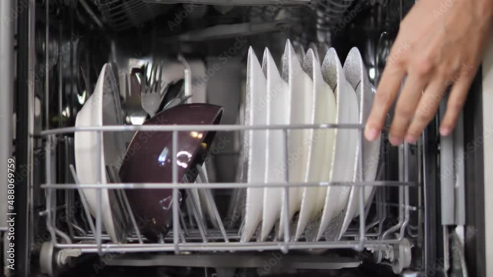 Adding dishes into the dishwasher machine. Arranged dishes into the