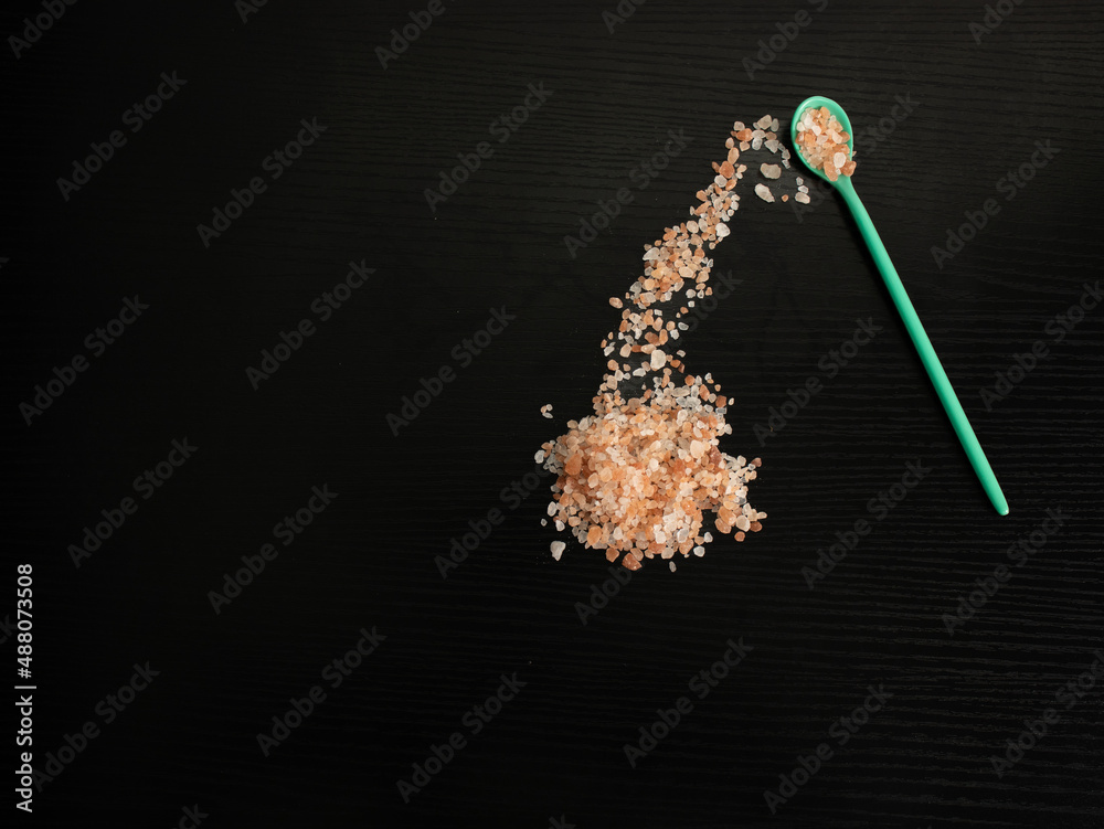 Himalayan pink salt, with a green teaspoon and a black background