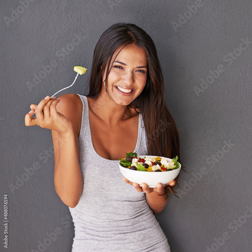 A bowl of my best salad ingredients. Portrait of a healthy young woman eating a salad against a gray background.