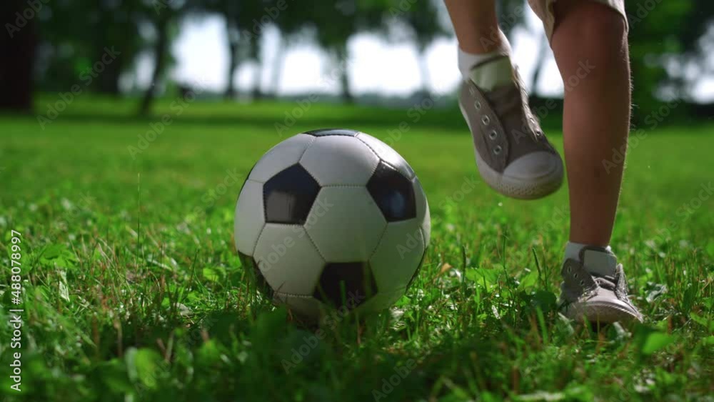 Closeup kid legs doing football tricks. Young player practice on green field. Closeup kid legs doing football tricks. Young player practice on green field.