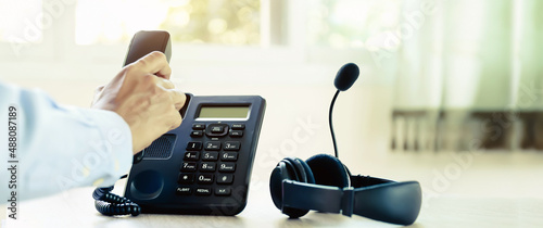 Customer service concept. Close-up telephone with hand holding and headphone for communication helpdesk IT support or call center and online services.