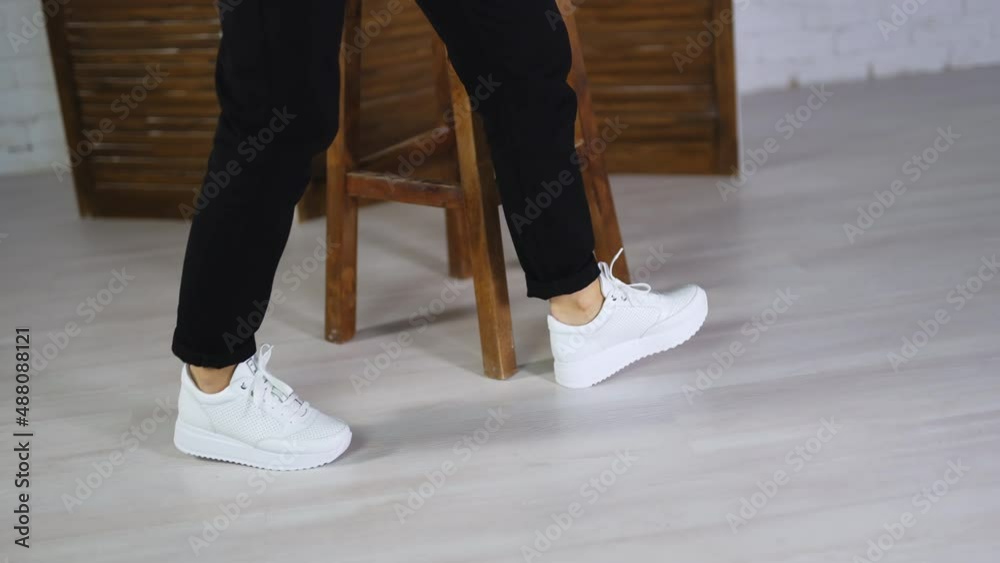 Woman wearing black trousers dances in white sneakers. New fashionable footwear demonstration concept. Woman wearing black trousers dances in white sneakers. New fashionable footwear demonstration concept.