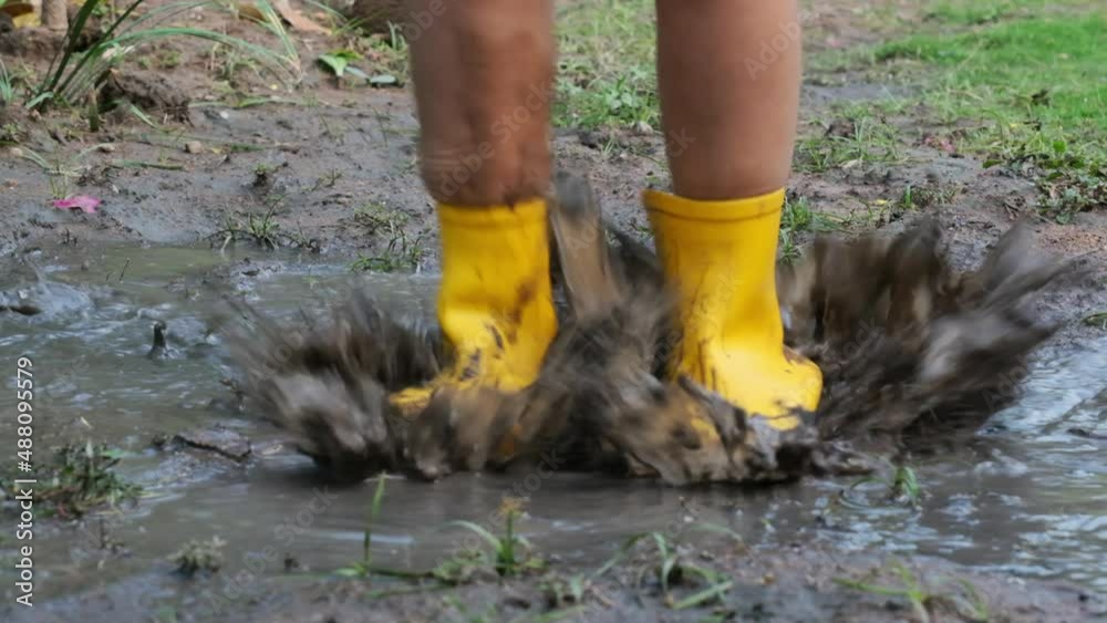 Close-up of the feet of a happy little girl in rubber boots jumping in ...