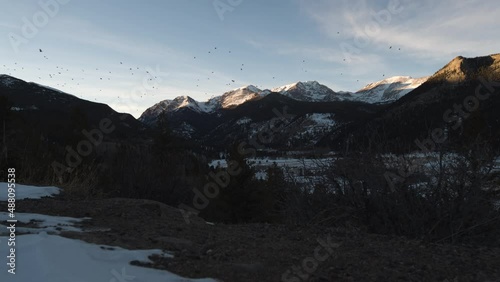 Birds flying in front of distant mountains as the sun is cresting the peaks in sunset