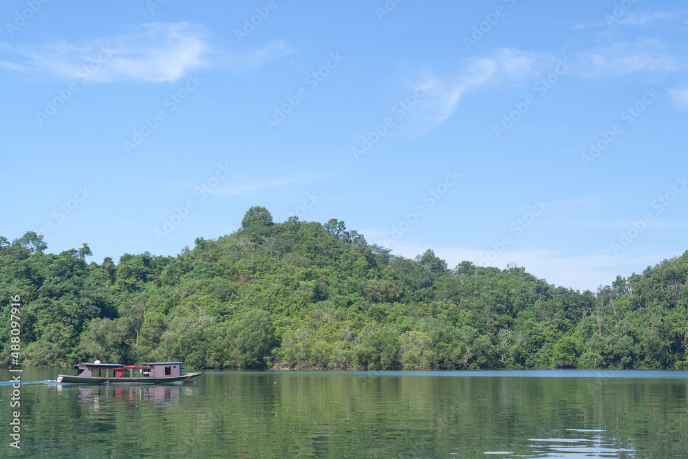 A small boat is seen crossing the hills in the morning with clear blue sky, on lake Aranio, South Borneo, Indonesia.