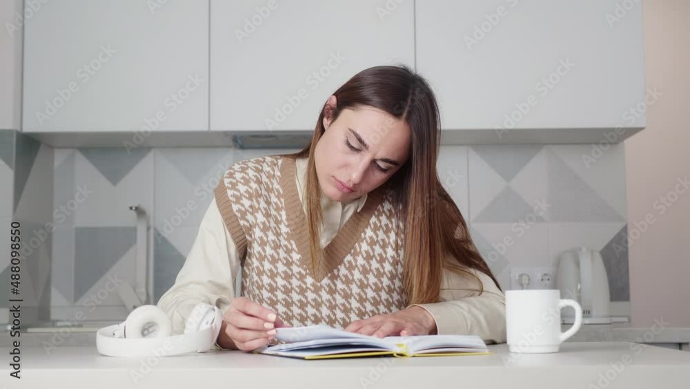 Close-up shot Young adult woman reading a book in the kitchen. Woman studying history Relaxing at home. Learning, knowledge, education, relaxing in daily life activities Close-up shot Young adult woman reading a book in the kitchen. Woman studying history Relaxing at home. Learning, knowledge, education, relaxing in daily life activities