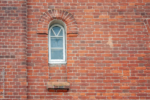 Window on the facade of an old house. Red brick wall with a window. Ancient brickwork and a lonely window on the wall.