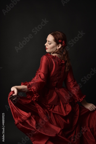 Photography portrait of pretty female model with red hair wearing glamorous historical victorian red ballgown