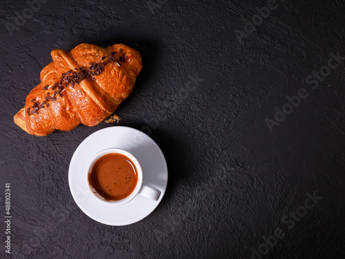 Fresh baked croissant, white mug of expresso on black concrete table. Cup of hot coffee, buns, rolls close up. Food, French breakfast, morning menu, cafe concept. Top view, copy space
