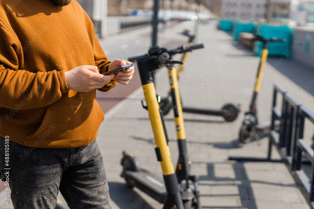 Close-up of male using smartphone after riding by electric scooter in the city. Innovative transport Close-up of male using smartphone after riding by electric scooter in the city. Innovative transport