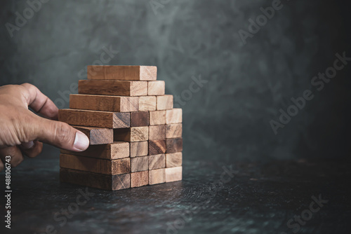 Hand pull wooden block stack in pyramid stair step concept of prevent collapse or crash of financial business and risk management or strategic planning and insurance.