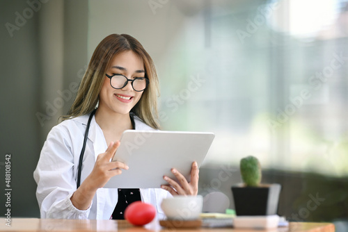 Smiling female doctor using digital tablet in bright modern hospital.