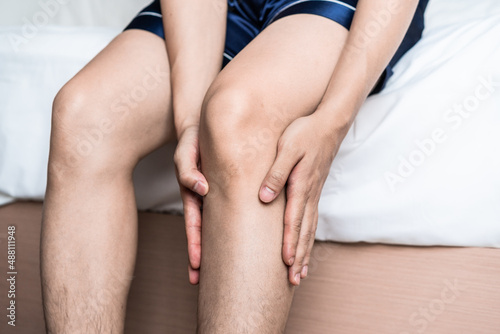 The man sitting in the bed  holding his knee with hands