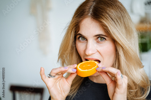 Portrait of a beautiful blonde woman eating an orange.girl gently holds the fruit in her hands. Catchy look of the lady. Girl and fresh fruit