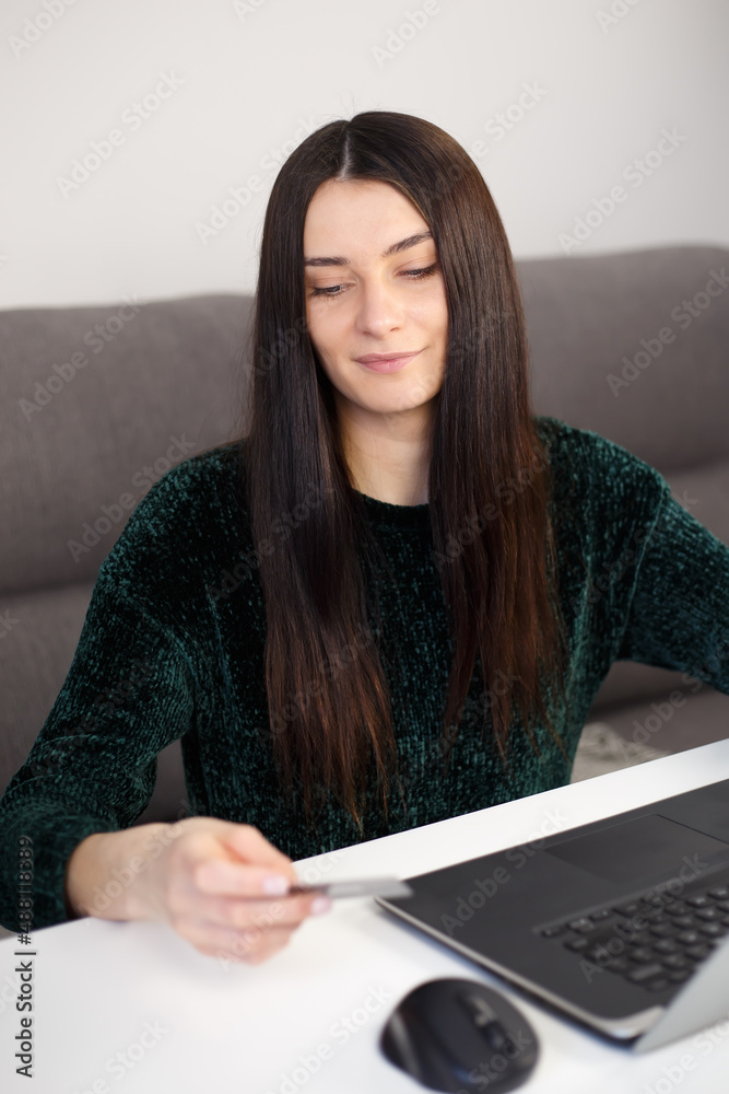 Woman making purchase online with credit card. Young white brunette makes money transfer with debit bank card and laptop computer connected to internet Woman making purchase online with credit card. Young white brunette makes money transfer with debit bank card and laptop computer connected to internet