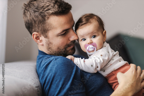 Father holding baby girl in arms while sitting on sofa. photo