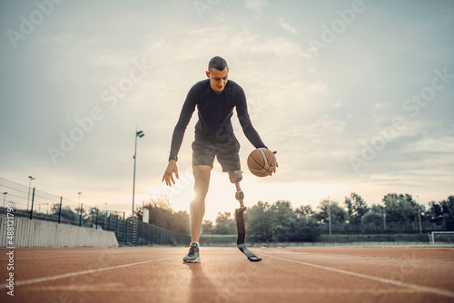 A handicapped sportsman with prosthetic leg practice basketball at stadium.
