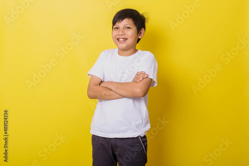 Smiling little boy crossing his arms isolated on yellow background