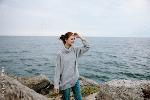portrait of a woman in a gray sweater stands on a rocky shore nature Lifestyle