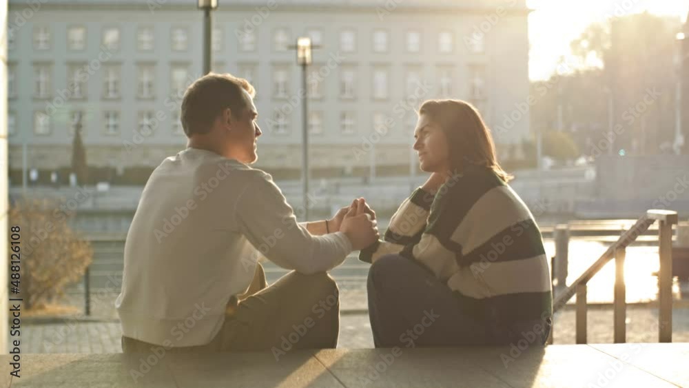 Romantic date on the waterfront. A pair of lovers sits on the city embankment and communicates cheerfully, the guy holds the girl's hand. Romantic date on the waterfront. A pair of lovers sits on the city embankment and communicates cheerfully, the guy holds the girl's hand.