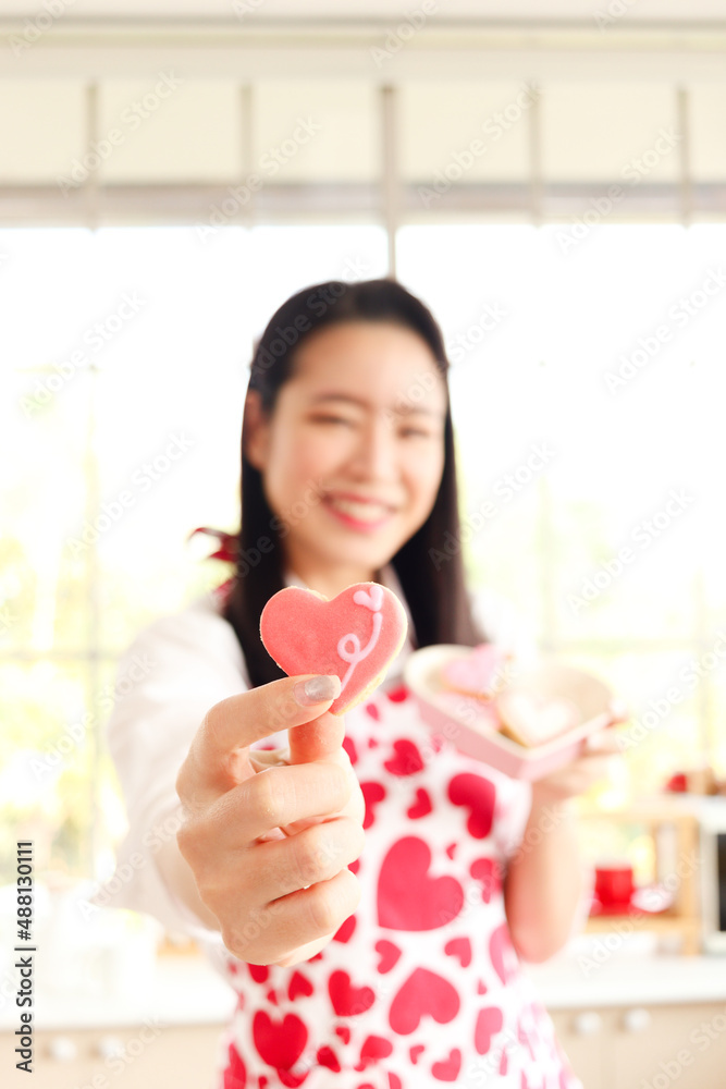 Happy smiling beautiful young Asian woman in cute red heart apron holding valentine homemade cookies, standing behind kitchen counter, preparing romantic love memorable anniversary celebration. Happy smiling beautiful young Asian woman in cute red heart apron holding valentine homemade cookies, standing behind kitchen counter, preparing romantic love memorable anniversary celebration.