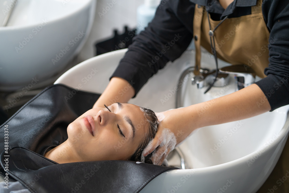 Fototapeta premium Beautiful Caucasian women feel relax and comfortable while getting hair wash with shampoo and massage. Hair salon studio with hair stylish, beauty and fashion concept.