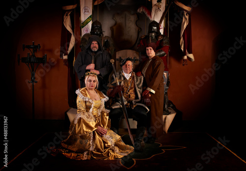 An elderly medieval count (baron, prince) sits on a throne in an ancient castle, next to his wife, daughter and warrior priest. Historical reconstruction in Saint Miklos castle in Ukraine