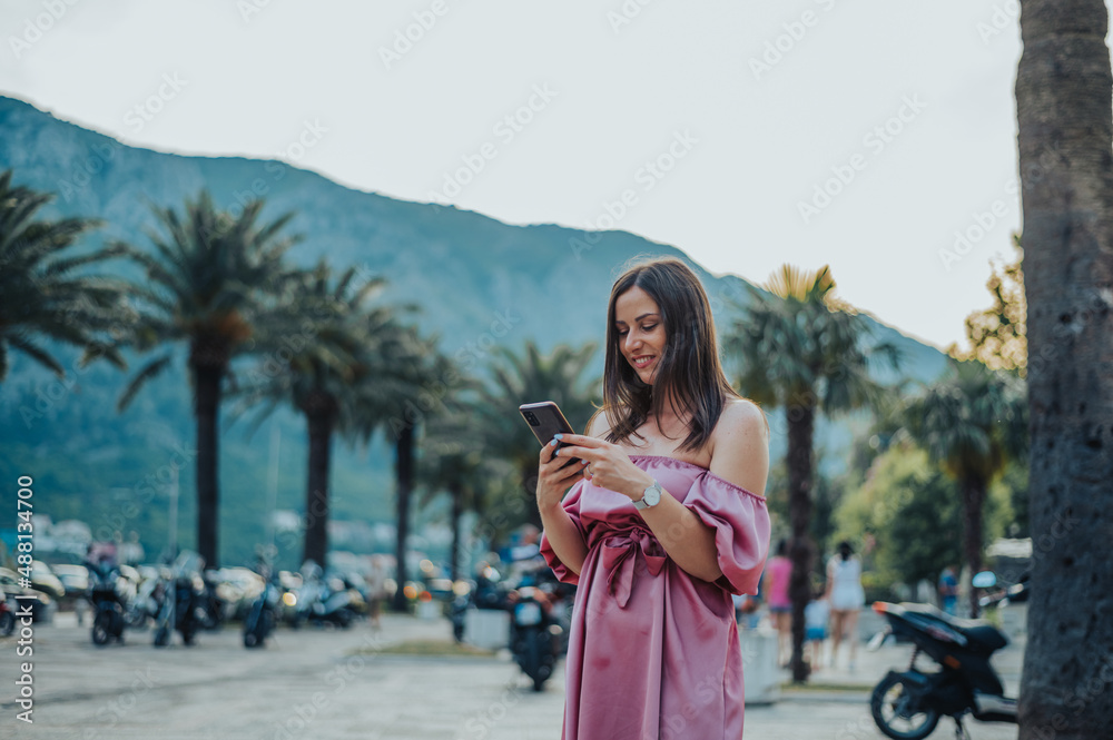 Beautiful young woman using smartphone while walking on the city streets on the coast